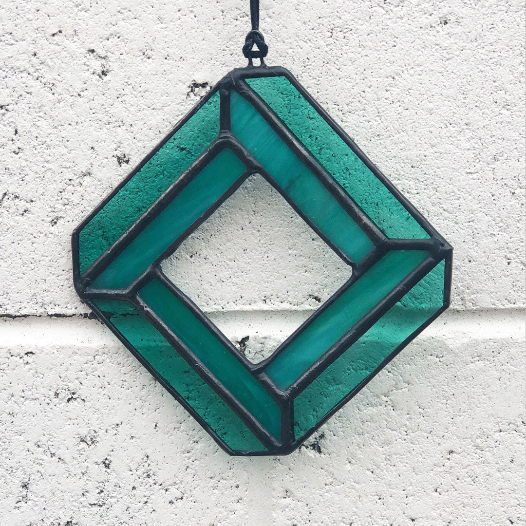 image of teal geometric diamond glass suncatcher on white brick background 