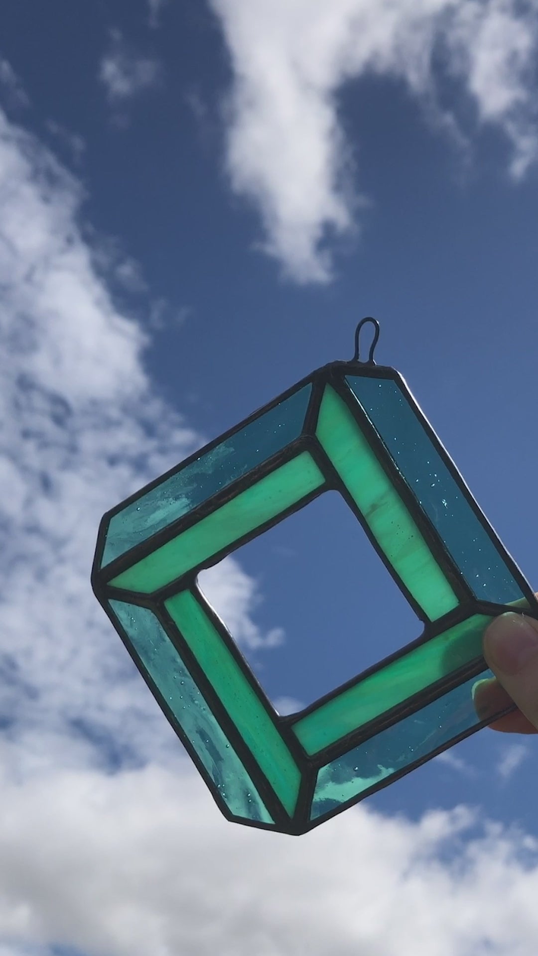 short video of image of teal geometric diamond glass suncatcher against a sunny sky