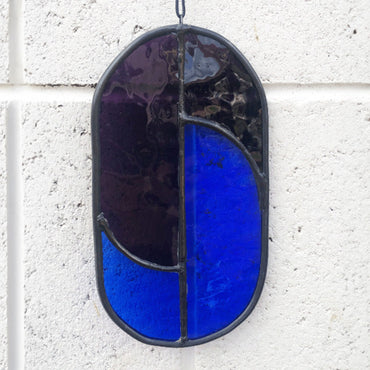 blue and purple suncatcher against a white brick wall, this shows the stained glass without the sun shining through it