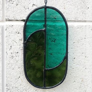 teal and green oval suncatcher against a white brick wall, this shows the piece without sunlight shining through