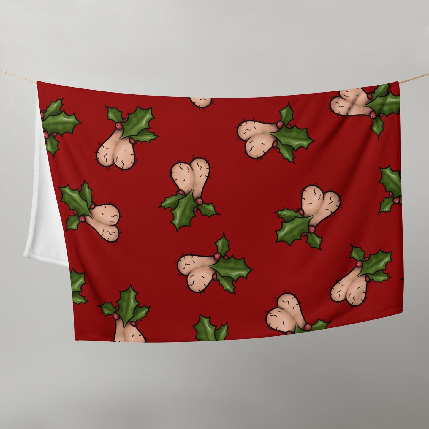 image of Jingle Balls blanket hanging in half on a clothes line to show size with repeated pattern image of Christmas testicles with holly and berries on a red background