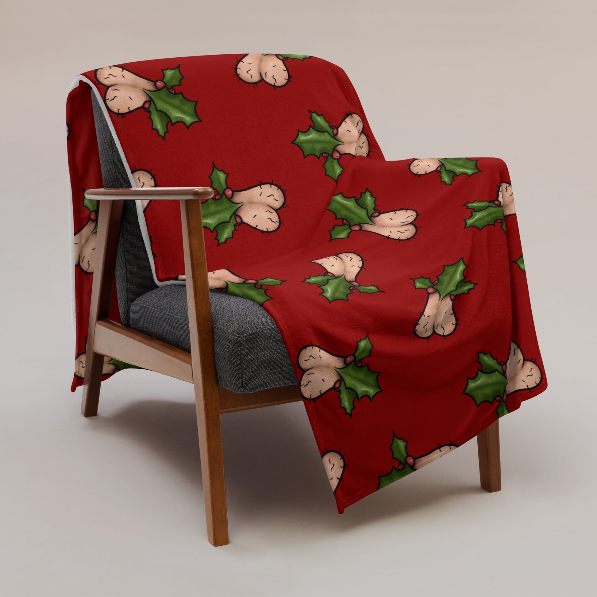 image of  Jingle Balls blanket draped over a chair with repeated pattern of Christmas testicles with holly and berries on a red background