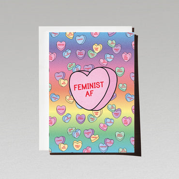 rainbow gradient background love greeting card with lots of candy hearts with female empowerment messages featuring one large pink candy heart with the text feminist a f