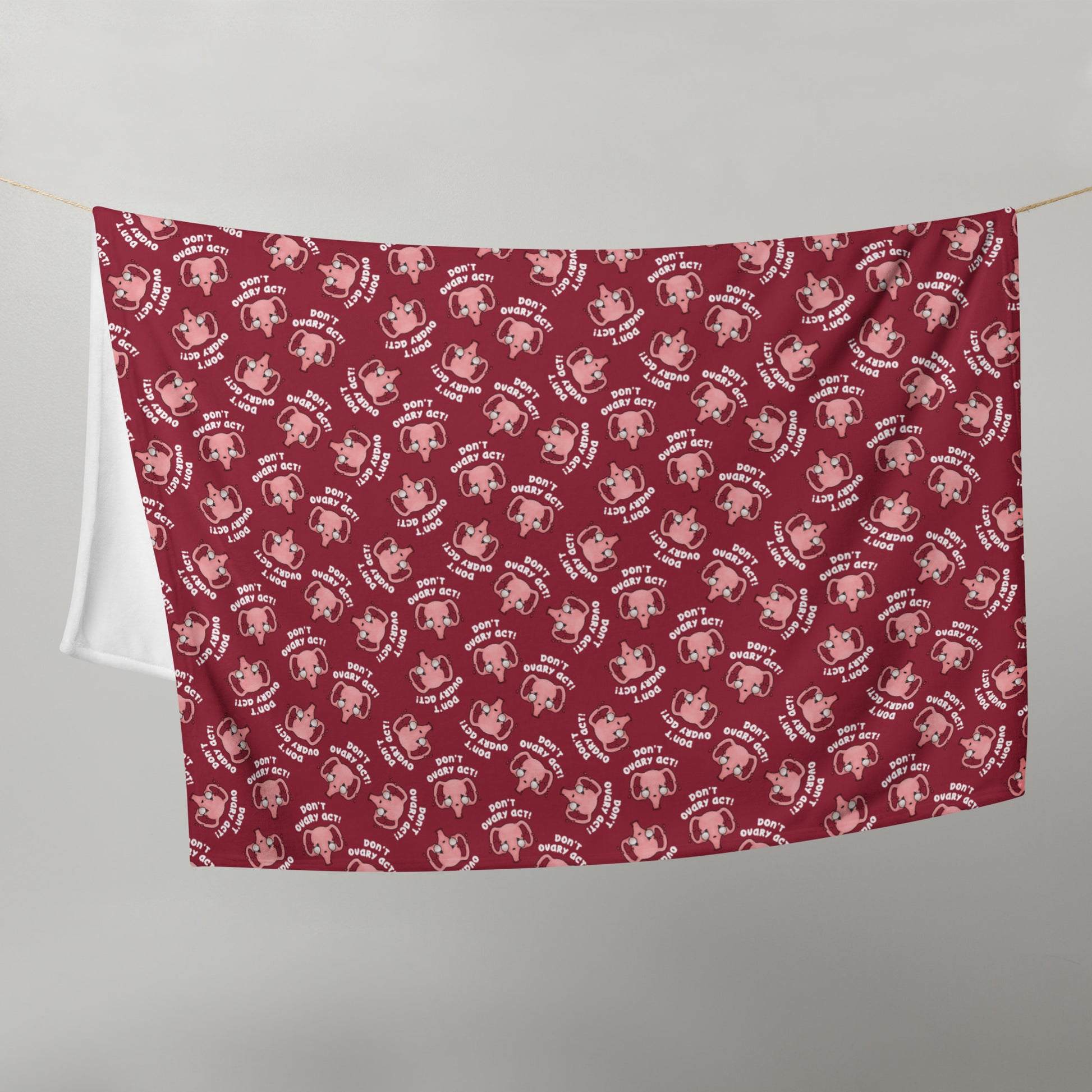 image of 50" x 60" red blanket hanging in half on a clothes line to show size with repeated pattern image of cute uterus characters crying and the text Don't Ovary Act